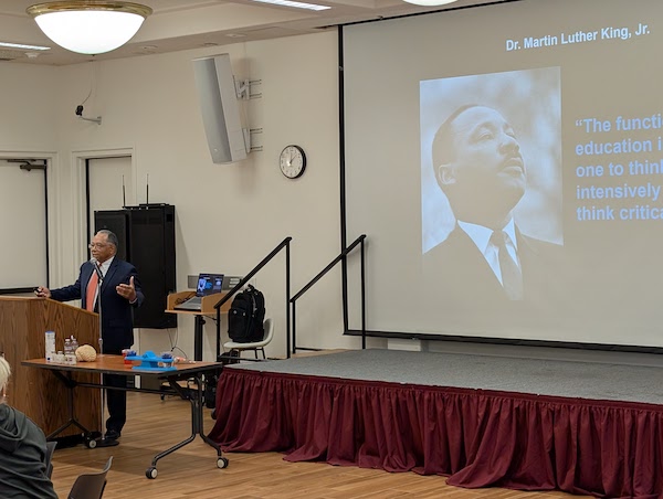 Man speaking at podium with MLKing image on screen behind him