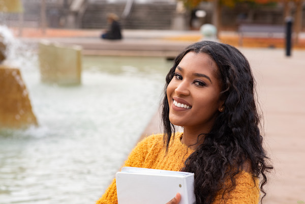 smiling young woman in mustard sweater in front of fountain