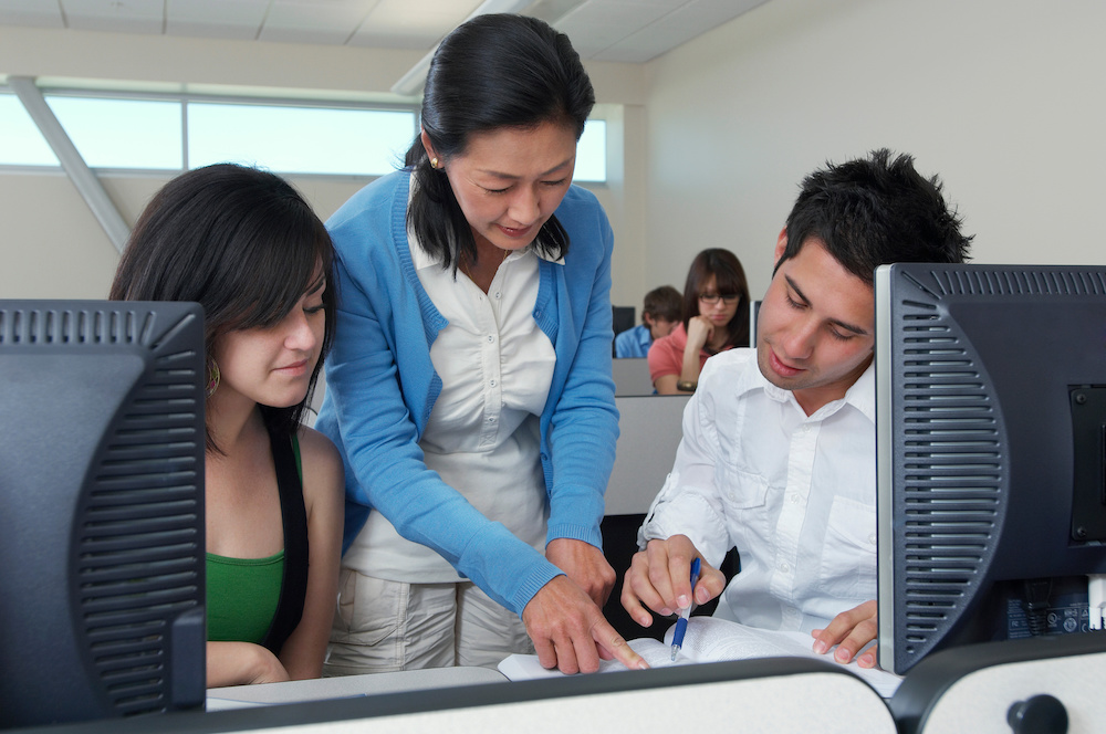 woman showing something to two college students at table